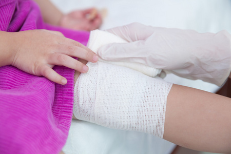 受伤的孩子.儿科医生包扎孩子的膝盖照片