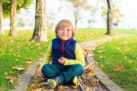 秋天的可爱的小男孩，其 4 岁的时候，玩着黄色的叶子在公园里，身穿蓝色夹克和绿色的裤子的肖像