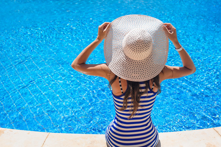 美丽的女人坐在游泳池边的帽子