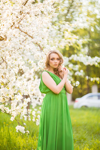 站在花朵盛开的苹果树旁边的漂亮年轻的金发女郎