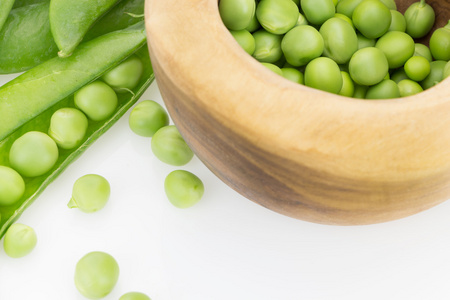新鲜的绿色豌豆荚和木碗的特写，白色背景上的豌豆