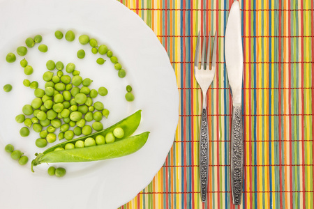 带刀和叉的特写，多彩竹餐垫上板的新鲜豌豆
