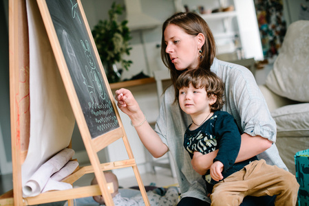 年轻的母亲和他的小儿子在黑板上画一支粉笔。 不是吗