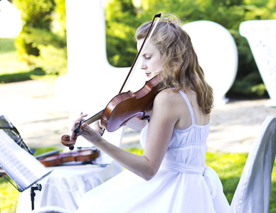 女孩在户外的小提琴演奏。婚礼的音乐家。小提琴在开阔的天空下