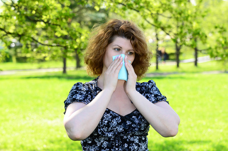 女人关闭用纸巾在公园里，鼻子花粉