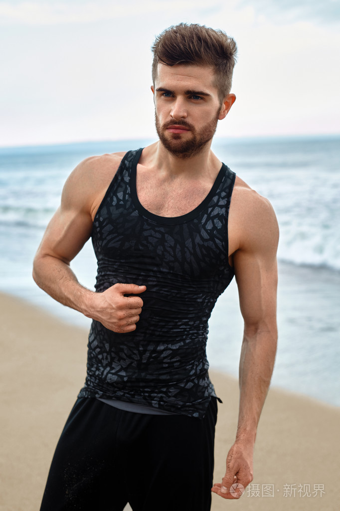 英俊的男人，与健康肌肉发达的身体，在海滩上的运动服