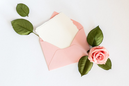 粉色信封与白卡和玫瑰。平躺