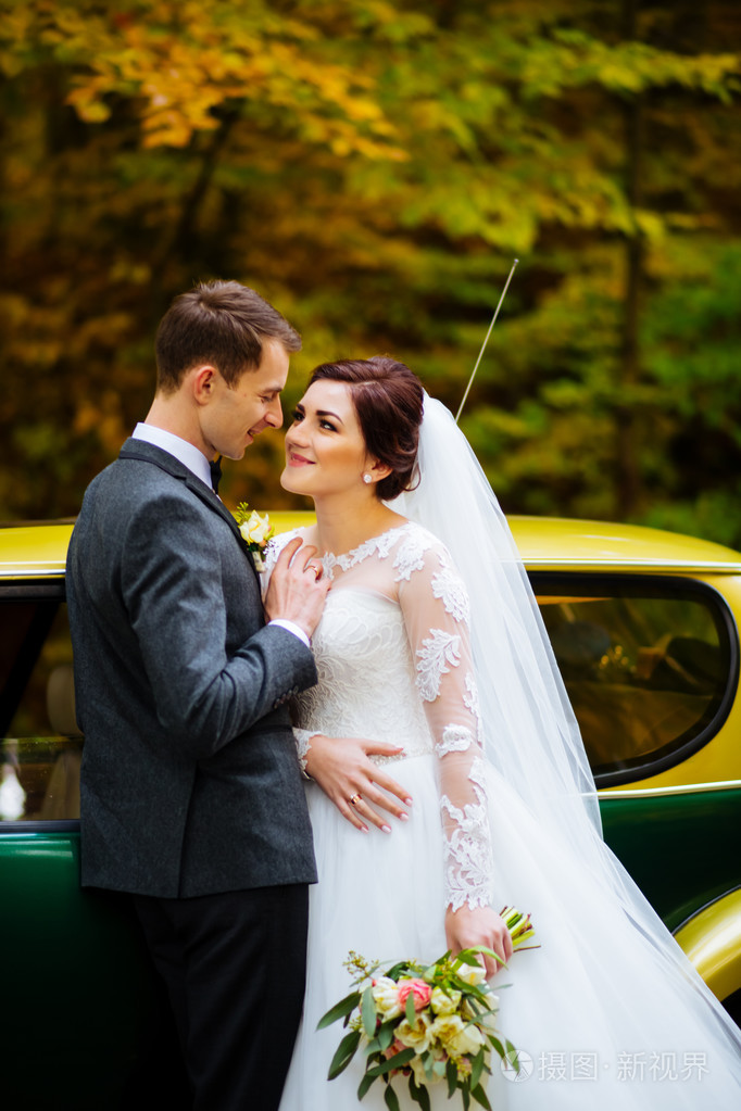 美丽幸福的年轻新娘接吻英俊的新郎,在阳光明媚的公园