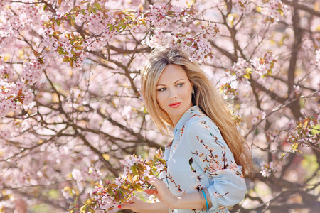 一件粉色樱花盛开在春天的背景上的蓝色连衣裙长发美丽年轻的金发女子的肖像