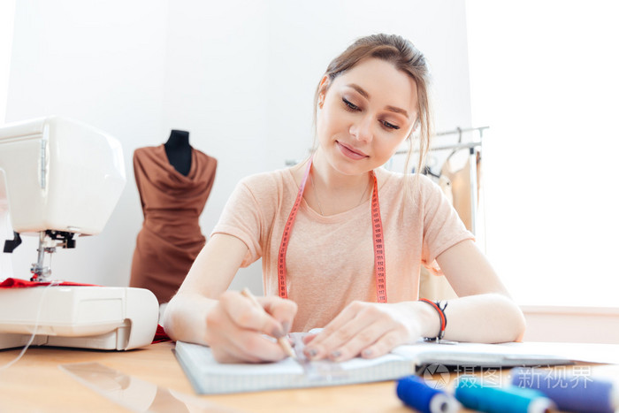 微笑的女人女裁缝绘图侧面在上班的笔记本