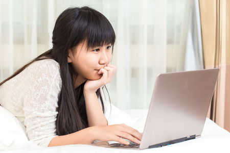 亚洲女人躺在床上在家里和她在一台笔记本电脑上工作