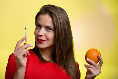 女人抱着一个注射器和一个橙子