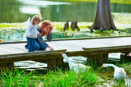 孩子们女孩和母亲玩鸭子在湖