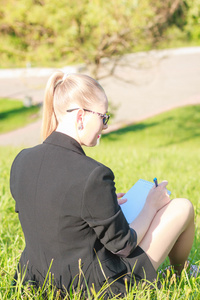 女人坐在草地上，在笔记本上书写