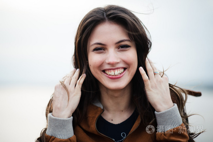 年轻快乐美丽漂亮的女性穿着皮革外套微笑着站在户外光线背景的特写