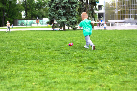 在绿色草地上踢足球的小男孩