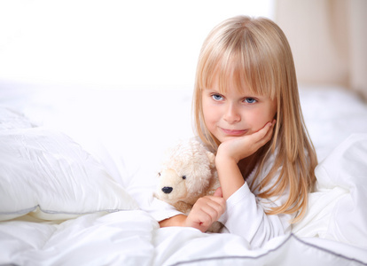 小女孩躺在家里的床上的玩具熊