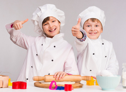两个笑的儿童，在厨房与竖起大拇指
