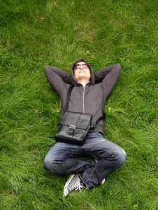 在绿色的草地上休息的休闲衣服的年轻男子