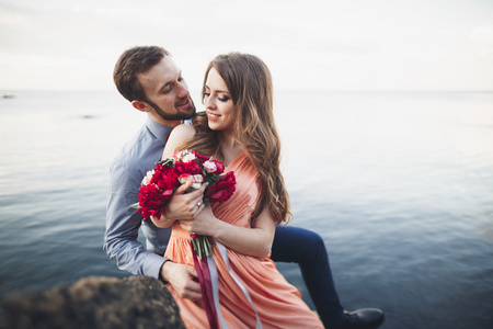 新婚夫妇坐在蓝色的海附近的大石头上