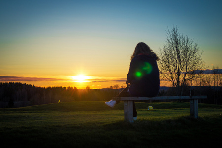 孤独的女孩，在日落时坐在板凳上