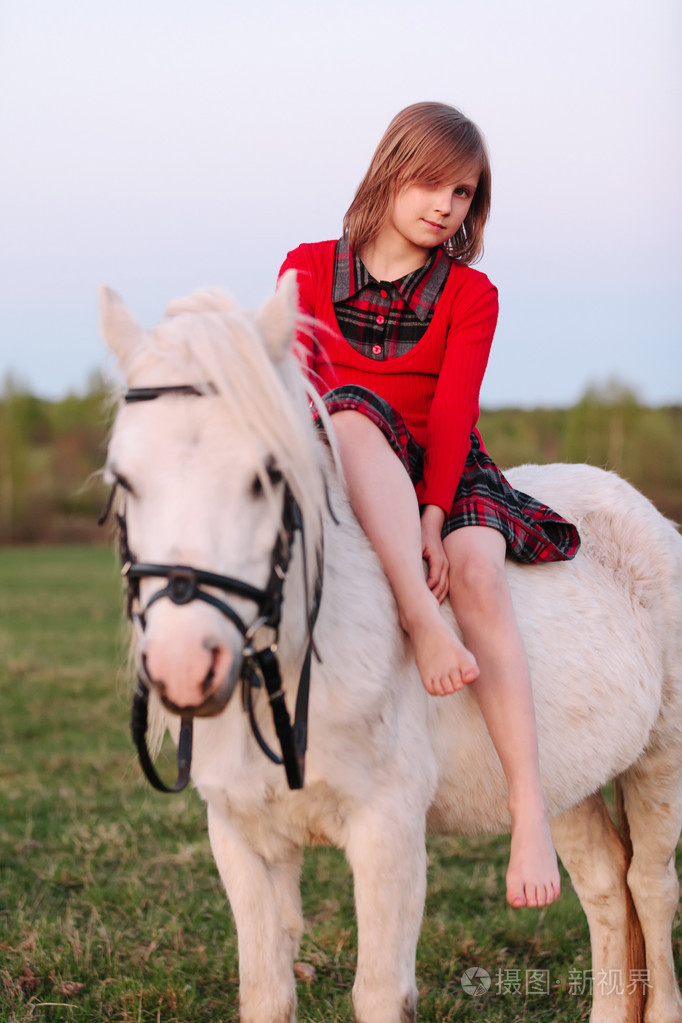 小的年轻女孩骑在一匹白马和微笑