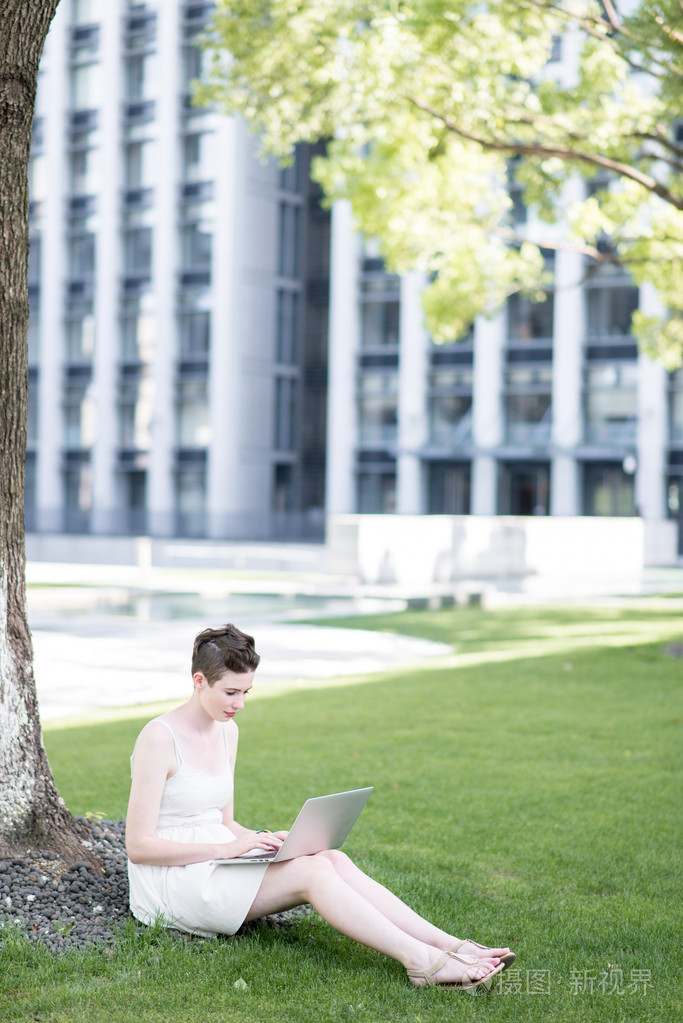 年轻女人使用平板电脑室外坐在草地上，微笑
