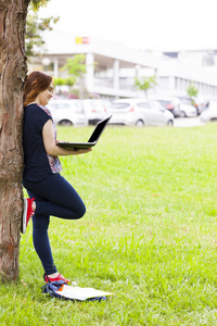 女学生使用一台笔记本电脑附近一棵树