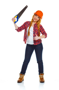 滑稽的年轻女人工人在用锯子锯在一张白纸的头盔