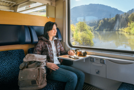 女人旅行坐火车和在上躺在表相机上的耳机听音乐。外面，美丽的景色