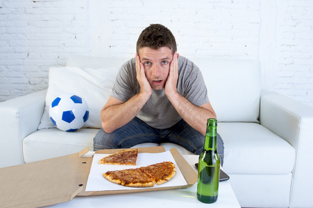 球迷在观看足球比赛的电视转播在沙发沙发与比萨饼盒子和啤酒瓶的应力