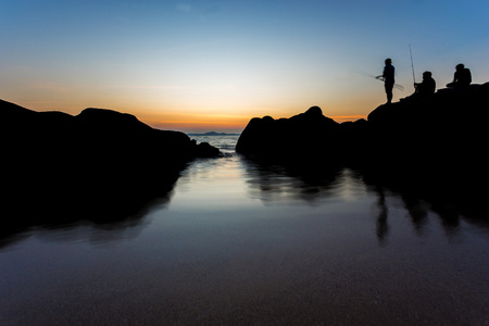 海景观和渔夫站在岩石海滩与夕阳 t