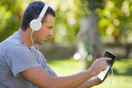 年轻人与戴着耳机的 tablet pc 听音乐放松公园