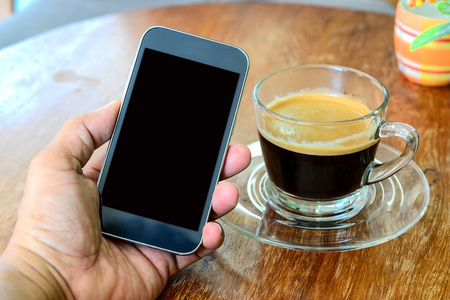 智能手机在手，木制的桌子上的咖啡