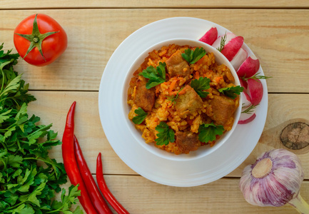 传统亚洲锋利抓饭用新鲜的香草 大蒜 胡萝卜和木制背景上的白色碗里的肉