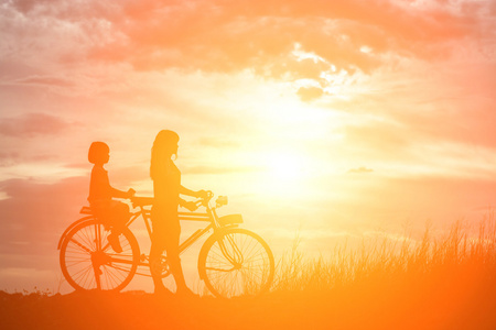 母亲和女儿骑自行车在夕阳的快乐时光的剪影
