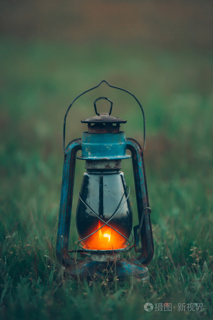 在日落时燃烧老式煤油灯站在绿色的草地上