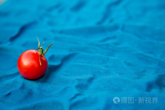 在蓝色的生动纺织的一个樱桃番茄。