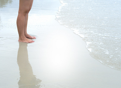 人的腿站在海滩与潮汐波