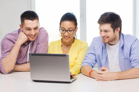 三个面带微笑的同事在办公室里拿着笔记本电脑