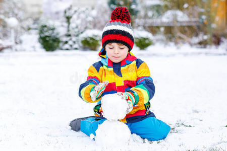 有趣的学龄前男孩穿着五颜六色的衣服堆雪人