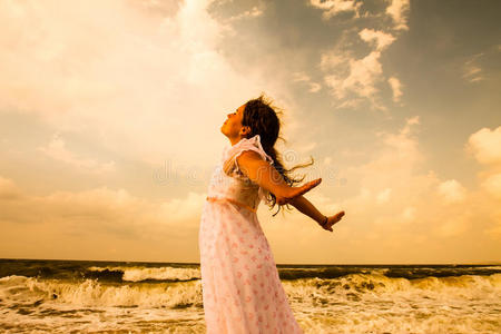 阳光明媚的海滩上穿着白色衣服的漂亮女孩。 自由与和平的概念