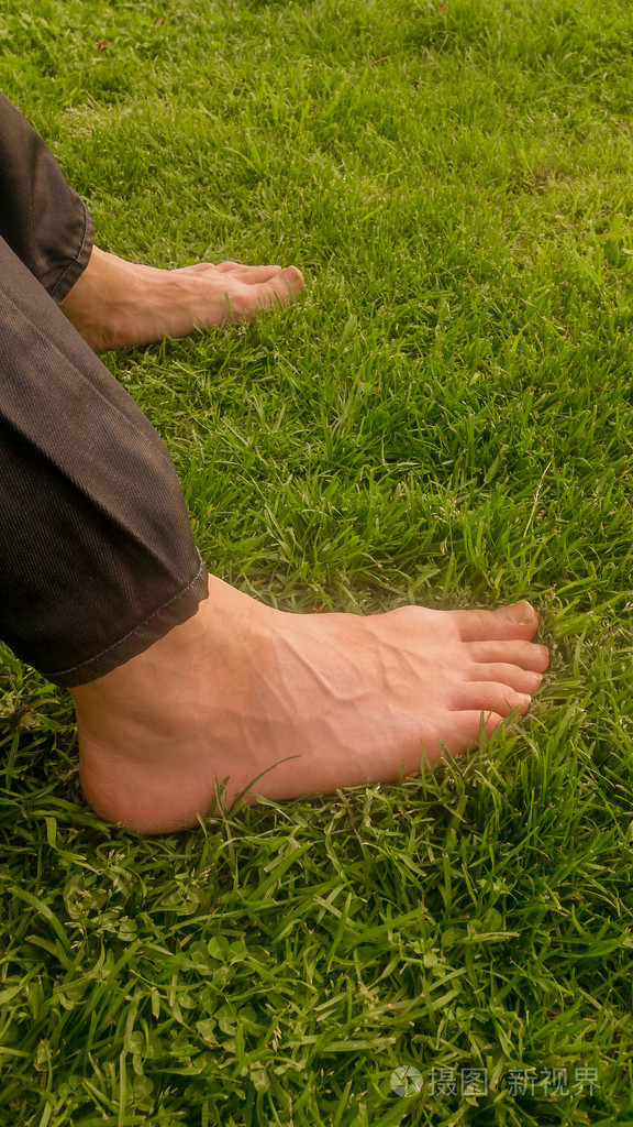 赤脚在太阳光下的绿草地上