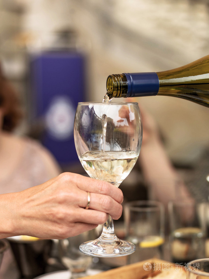 把白葡萄酒倒入一只手紧紧握着的杯子里