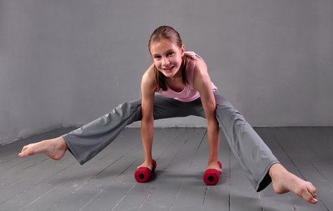 十几岁的女孩与哑铃,研制与哑铃锻炼肌肉在灰色的背景上.