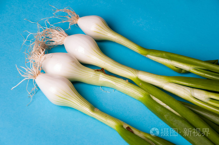 与茎在从上面的蓝色背景上的新鲜年轻洋葱