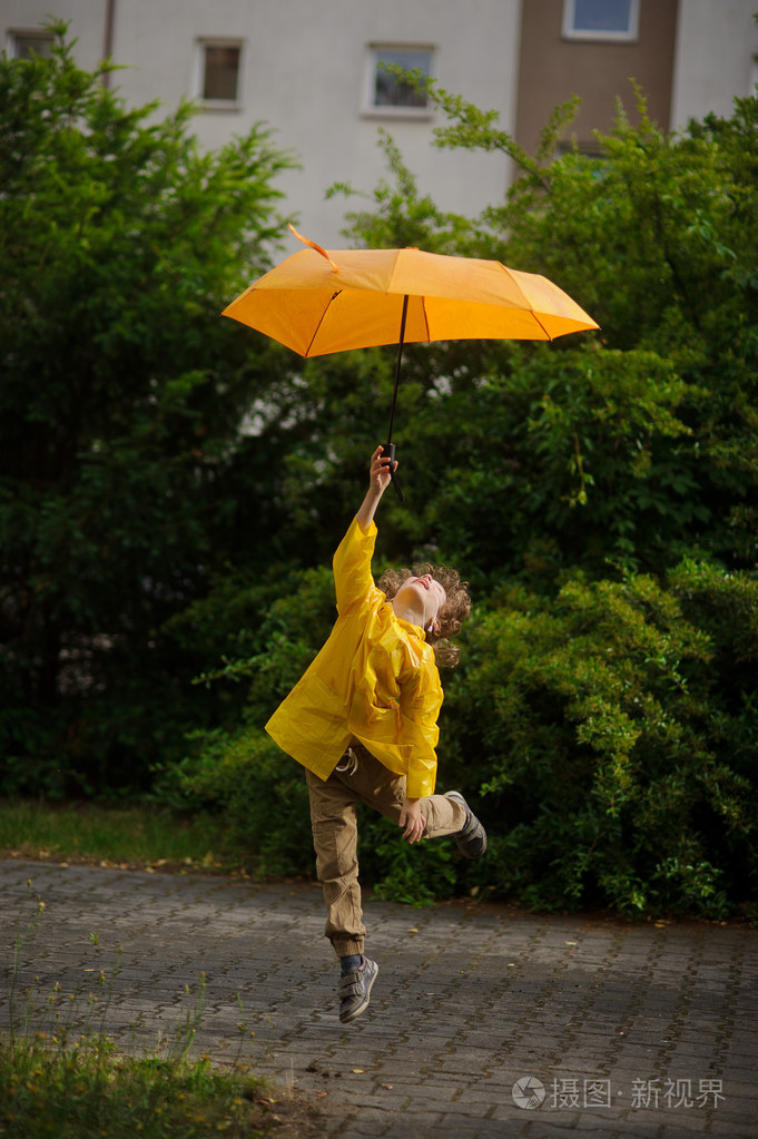 穿亮黄色雨衣的男孩手里拿着雨伞飞过地球.