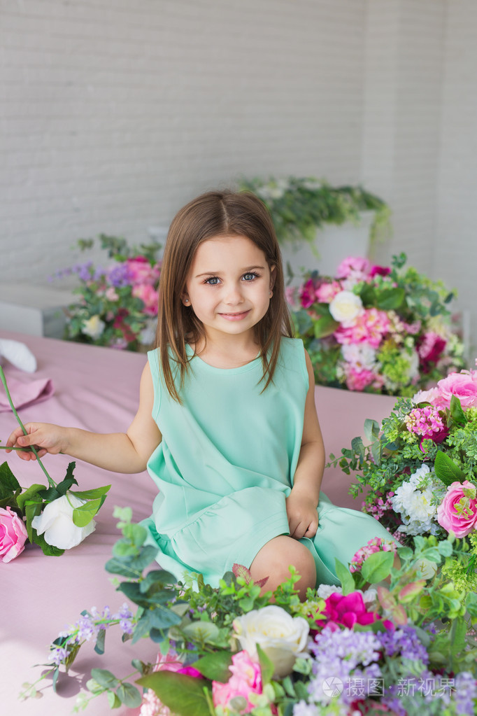 在附近的一个摄影棚里的花的绿松石裙子的漂亮的小女孩的肖像