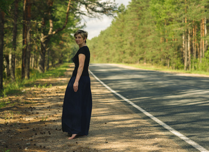 沿着这条路走的年轻女人和森林背景再回头看照片