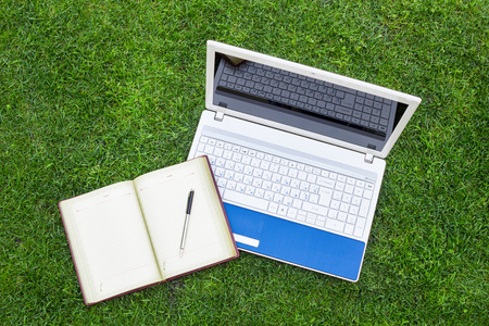 金属手提电脑白色手提电脑, 笔记本和笔放在绿色的草田照片